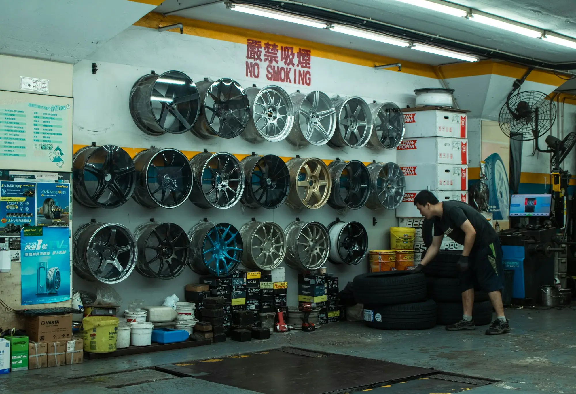 Worker stacking tyres in an auto shop with car wheels displayed on the wall